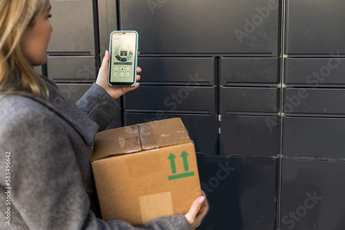 Beautiful woman picking up a package from a smart electronic steel parcel locker box, automatic mailboxes. Paczkomat delivery service, collection machine photo