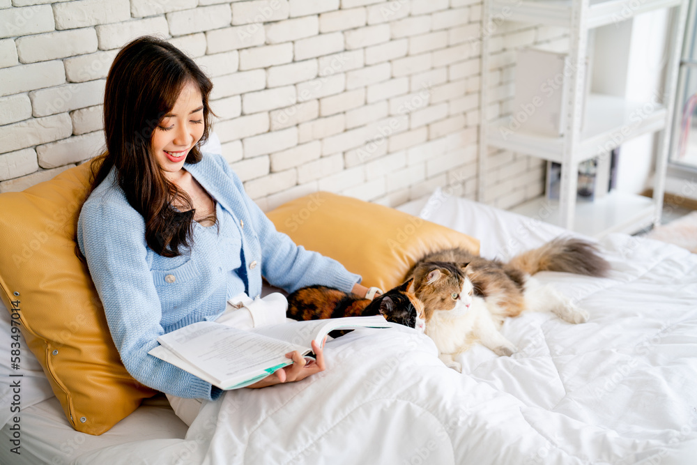 Asian woman sit on bed and relax by read the book also stay and pet her cat in bedroom in concept of good relationship and bonding between owner and pet. Asian woman sit on bed and relax by read the book also stay and pet her cat in bedroom in concept of good relationship and bonding between owner and pet.