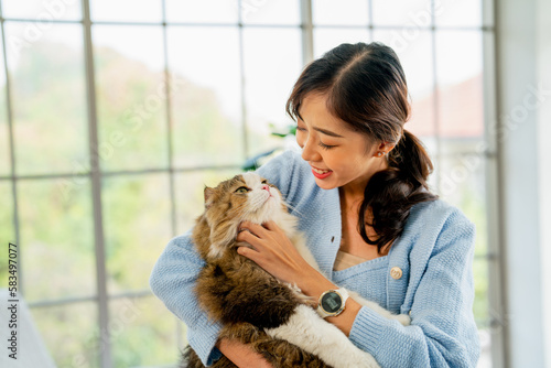 Asian woman hold and teasing fluffy cat while cat look relax and enjoy and woman look happiness to stay and enjoy with her pet.