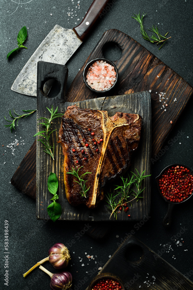 grilled medium-rare beef steak on a T-bone on a wooden board with rosemary. On a dark slate background. grilled medium-rare beef steak on a T-bone on a wooden board with rosemary. On a dark slate background.