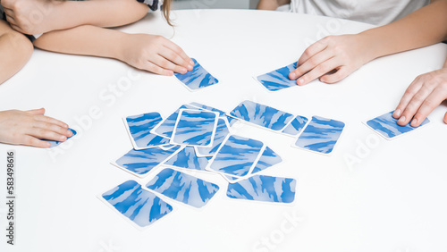 Cropped unrecognizable close up children hands holding blue playing cards on white table. Card game for time. Opposition and funny activity. Gambling, logical and motor games for family and company.