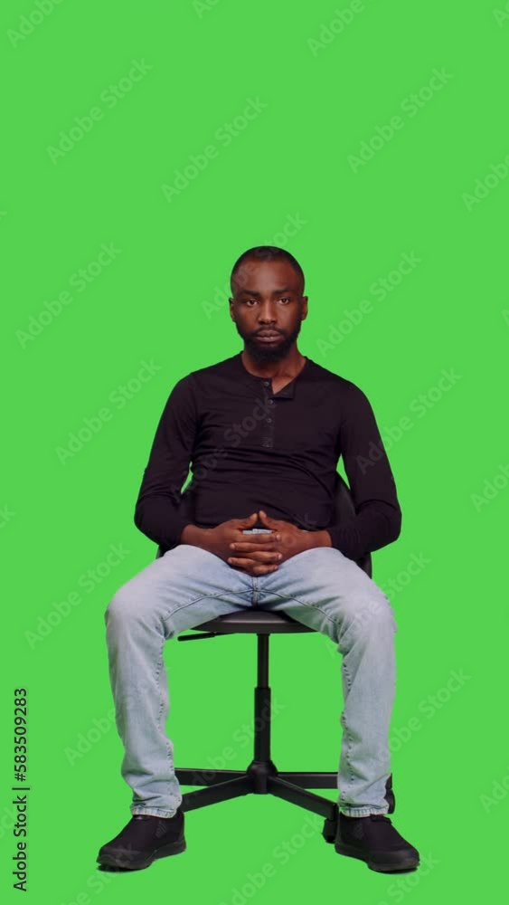 Vertical video: Front view of african american person waiting for something on chair, sitting over full body green screen backdrop. Young male model feeling confident and optimistic on camera, casual Vertical video: Front view of african american person waiting for something on chair, sitting over full body green screen backdrop. Young male model feeling confident and optimistic on camera, casual