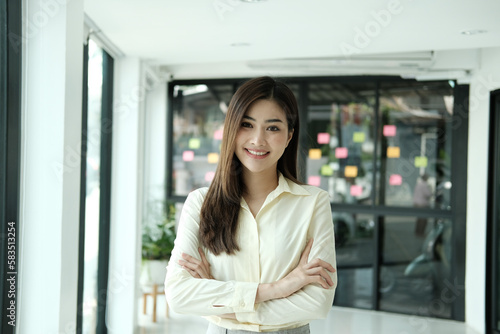 Young confident smiling Asian business woman leader, successful entrepreneur, elegant professional company executive ceo manager, wearing suit standing in office with arms crossed. Portrait