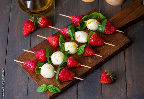 Strawberry Caprese Skewers. Lemon olive oil marinated mozzarella mini balls with fresh basil leafs and strawberries threaded on skewers served on a wooden board. Selective focus, horizontal. photo