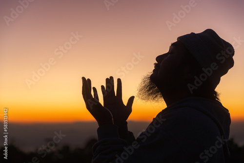 Silhouette of man kneeling down praying for worship God at sky background. Christians pray to jesus christ for calmness. In morning people got to a quiet place and prayed. copy space.