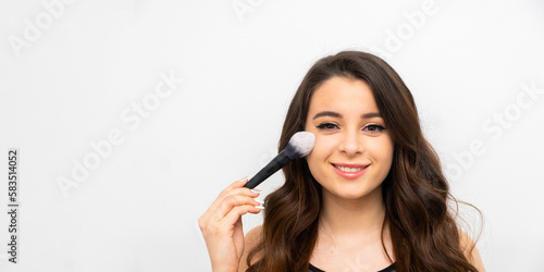 Portrait of cheerful laughing woman applying powder on her cheek with a brush. Skincare and cosmetic procedures. 