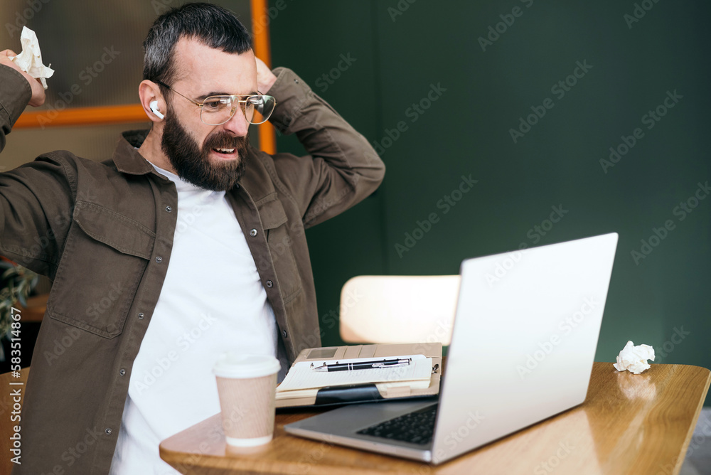 Angry caucasian male freelancer in a cafe quarreling while talking on webcam, discussing problems with an online business project, crumpling notebook pages Angry caucasian male freelancer in a cafe quarreling while talking on webcam, discussing problems with an online business project, crumpling notebook pages