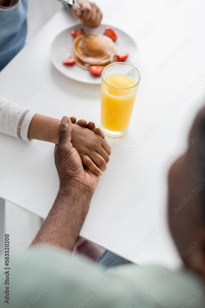 top view of african american girl holding hands with grandfather during breakfast. top view of african american girl holding hands with grandfather during breakfast.