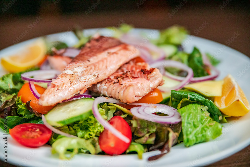 Shot of a salat vegan dish on a white plate with salmon on top. very colorfull dish healthy vegetarian with salmon fish