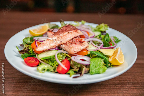 Shot of a salat vegan dish on a white plate with salmon on top. very colorfull dish healthy vegetarian with salmon fish