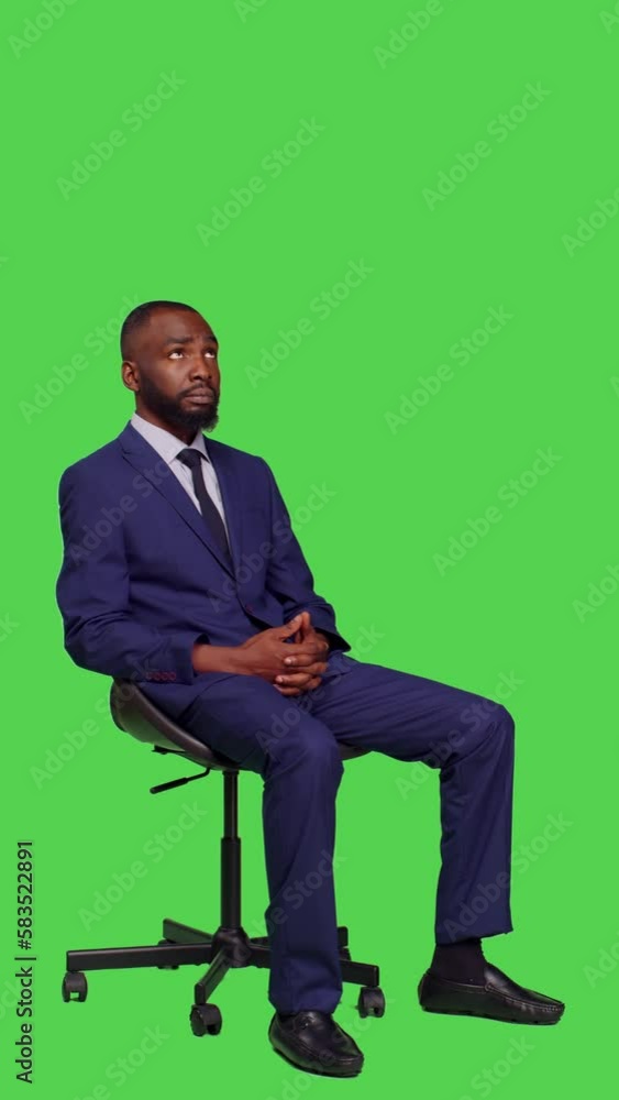 Vertical video: Side view of male company entrepreneur sitting on chair in studio, wearing business suit and posing over full body green screen. Young office worker feeling confident on camera Vertical video: Side view of male company entrepreneur sitting on chair in studio, wearing business suit and posing over full body green screen. Young office worker feeling confident on camera