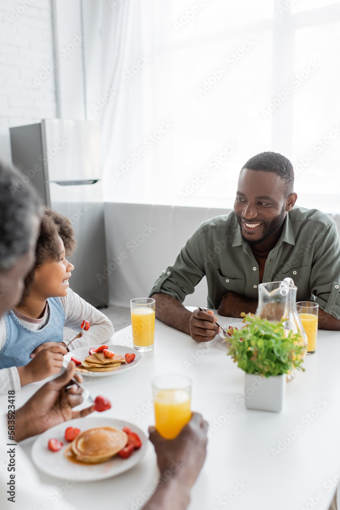 happy african american girl looking at cheerful father while having family breakfast. happy african american girl looking at cheerful father while having family breakfast.