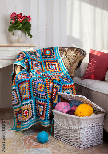 Bright beautiful hand-knitted plaid on a wicker chair and a basket with colored yarn