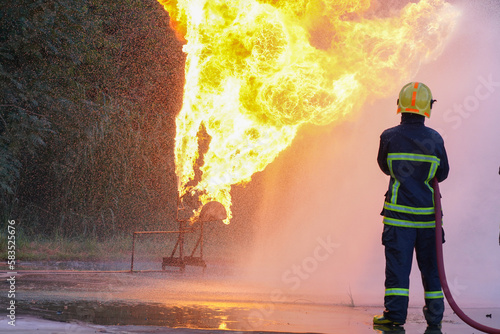 irefighters using Twirl water fog type fire extinguisher to fighting with the fire flame from oil to control fire not to spreading out. Firefighter and industrial safety concept.
