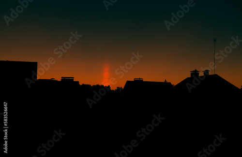 a natural phenomenon of a light column. visual atmospheric phenomenon, optical effect, sunlight refracting in the air at sunset beautiful sunset sky over the roofs of houses.banner,poster.dramatic sky © Viktorya 