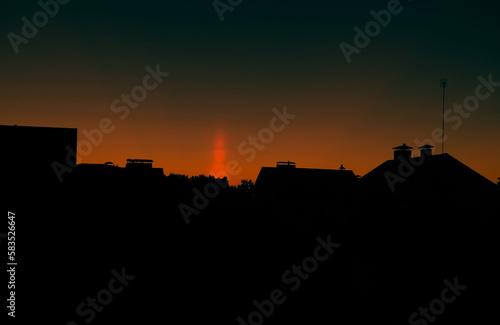 a natural phenomenon of a light column. visual atmospheric phenomenon, optical effect, sunlight refracting in the air at sunset beautiful sunset sky over the roofs of houses.banner,poster.dramatic sky