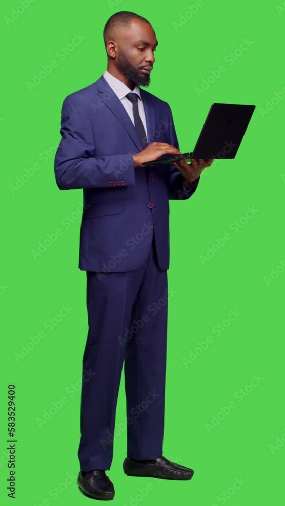 Vertical video: Side view of confident manager using laptop to browse internet, looking at online web page over full body green screen backdrop. Male entrepreneur working with portable computer on Vertical video: Side view of confident manager using laptop to browse internet, looking at online web page over full body green screen backdrop. Male entrepreneur working with portable computer on