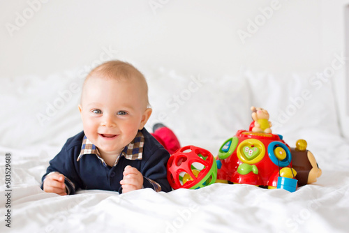 Sweet toddler boy, playing with colorful toys in bed photo