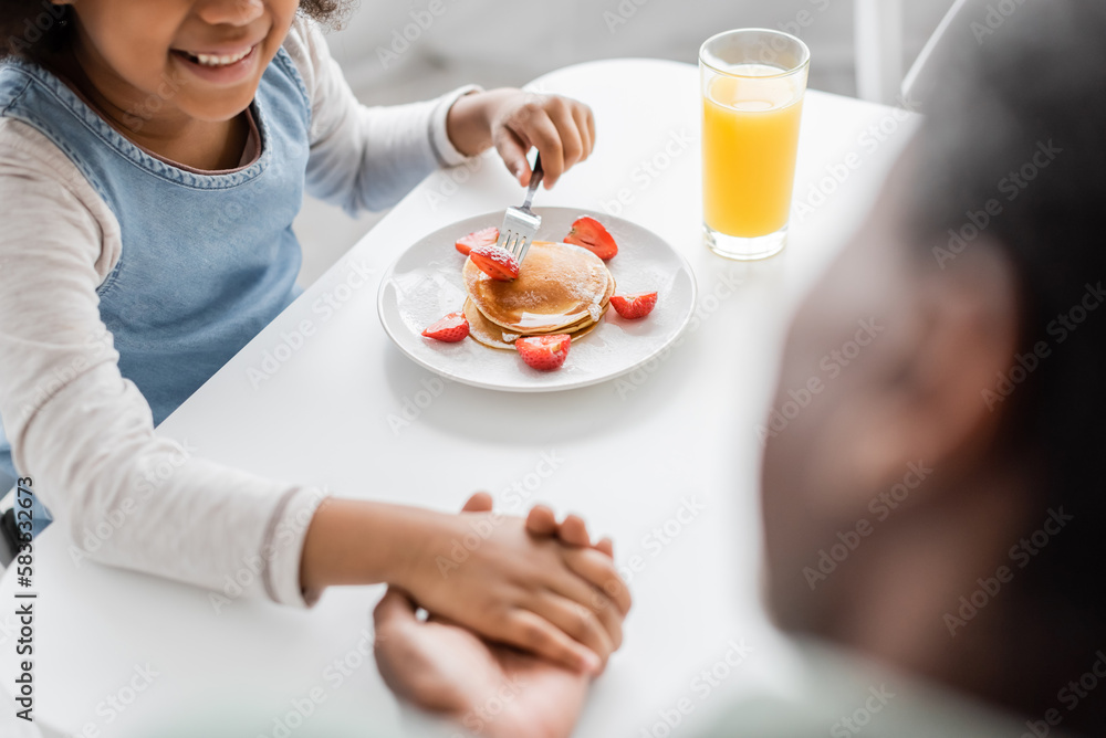 high angle view of happy african american girl holding hands with grandfather during breakfast. high angle view of happy african american girl holding hands with grandfather during breakfast.