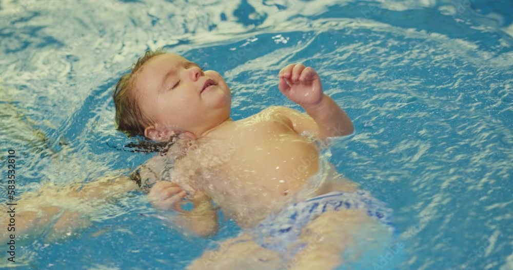 Father holding little baby and helping to swim in swimming pool with clean blue water. Professional water therapy for kids . Swimming training from an early age . Parent having fun . Happy lifestyle Father holding little baby and helping to swim in swimming pool with clean blue water. Professional water therapy for kids . Swimming training from an early age . Parent having fun . Happy lifestyle