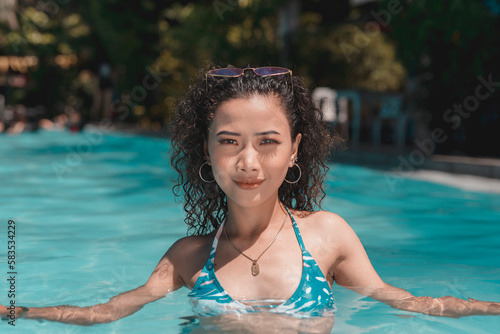 A young asian woman with curly hair relaxing in chest deep waters in the swimming pool. Enjoying her summer vacation. © Mdv Edwards