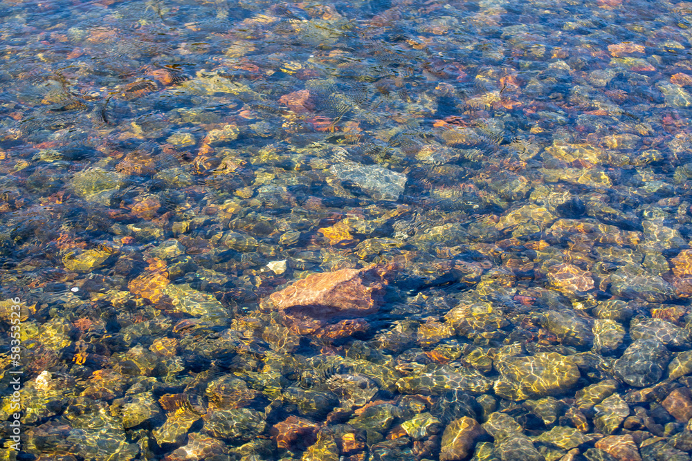 Small stones at the bottom of the river under a layer of clear water. Background from stones. Texture of water and stones.