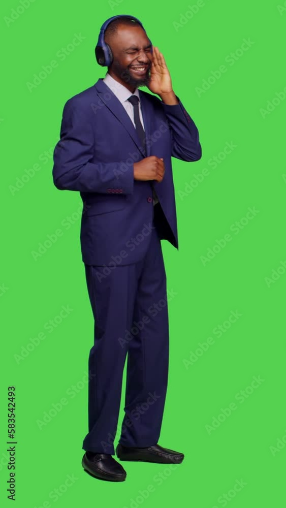 Vertical video: Side view of male manager using headset listening to music on camera, having fun with radio songs over full body green screen. Young businessman in suit dancing and wearing headphones Vertical video: Side view of male manager using headset listening to music on camera, having fun with radio songs over full body green screen. Young businessman in suit dancing and wearing headphones