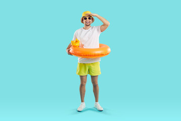 Funny joyful young man set up for summer vacation and looking for good offer from travel agency. Happy guy in summer clothes and with inflatable circle looking into distance on light blue background.