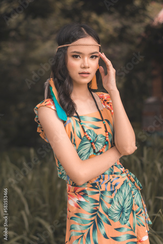 A Pensive young teenage woman in boho style tropical outfit, in deep thought. Outdoor shot, warm tones.