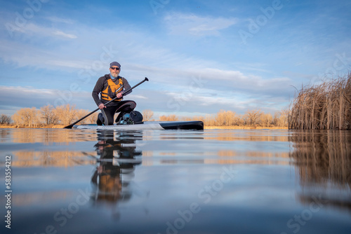 senior paddler and his paddleboard on lake in winter or early spring in Colorado, frog perspective (partially submerged action camera)