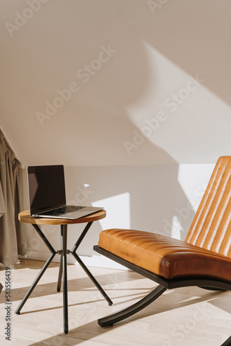 Minimalist modern home office workspace interior design concept. Leather armchair  laptop computer on side table. Aesthetic soft sunlight shadows on the wall