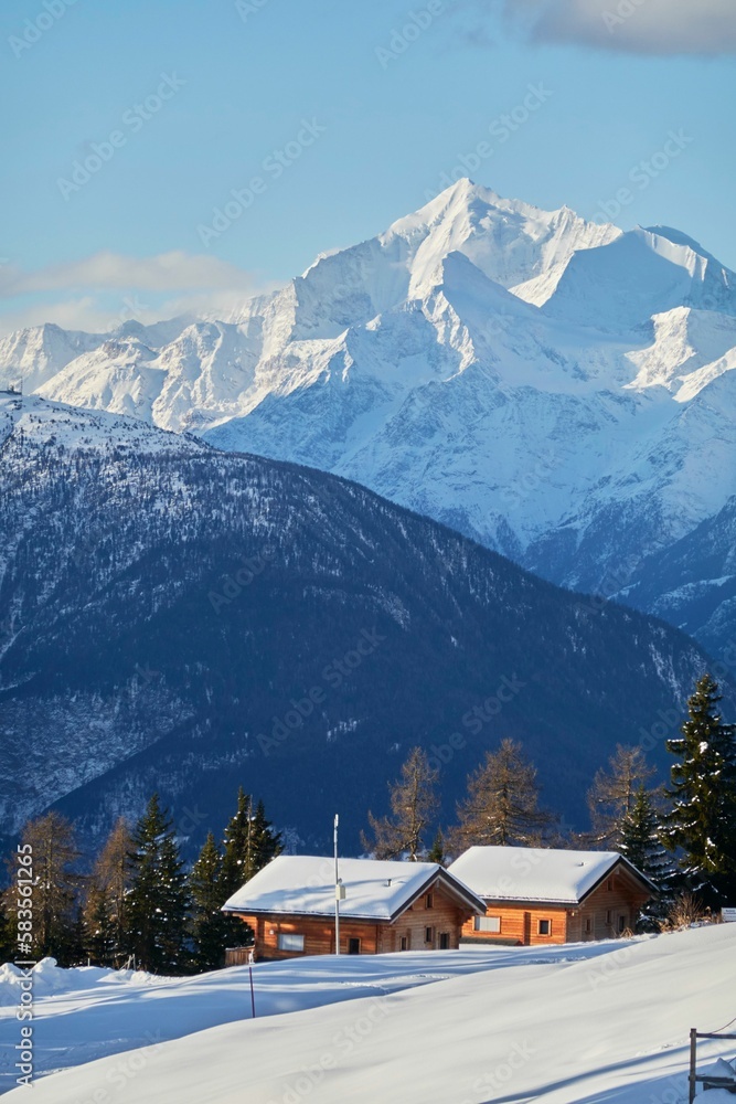 Fototapeta premium Vertical shot of the small huts nestled between the snowy mountains