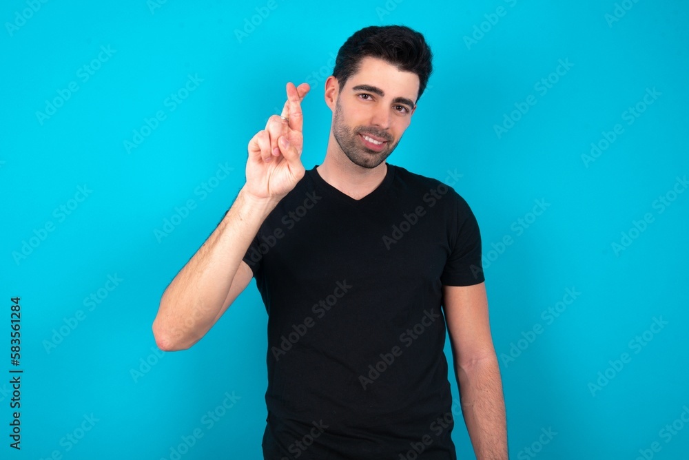 Young man wearing black T-shirt over blue studio background pointing up with fingers number ten in Chinese sign language Shi Young man wearing black T-shirt over blue studio background pointing up with fingers number ten in Chinese sign language Shi