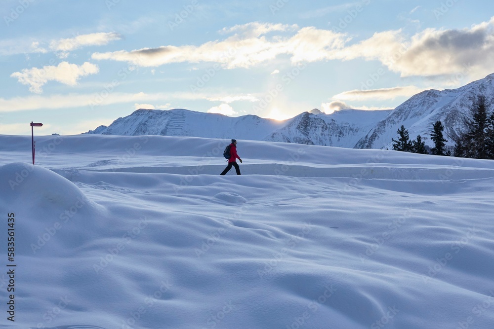 Man hikes snowy trails in Swiss Alps at dawn in winter