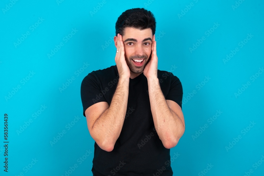 Young man wearing black T-shirt over blue studio background Pleasant looking cheerful, Happy reaction