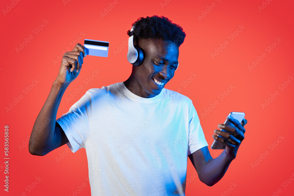 Cheerful black guy using smartphone, headphones and bank card Cheerful black guy using smartphone, headphones and bank card