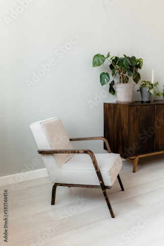 Beige armchair and wooden chest of drawers with house flowers. mid-century modern style