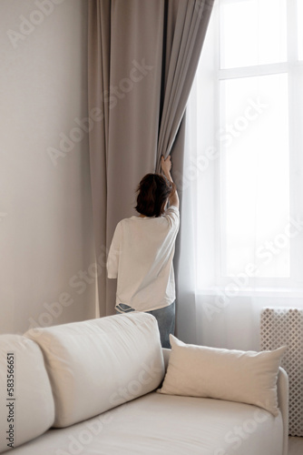 The girl opens the curtains in the apartment