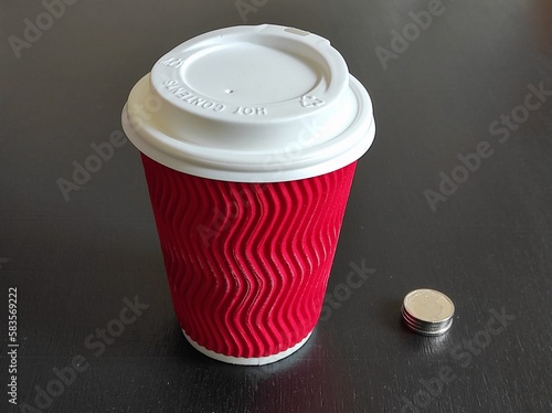 Red paper cup with several shiny coins next to it on a black background