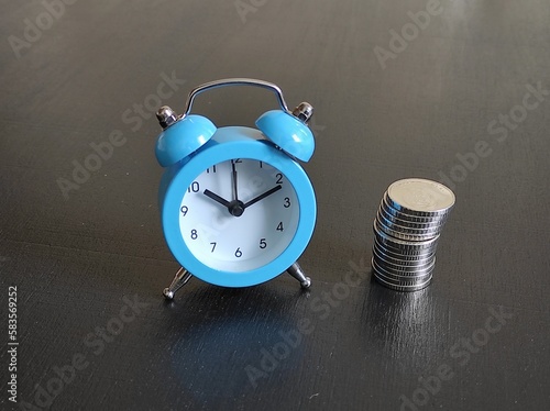 Clock and a column of shiny coins on a black background