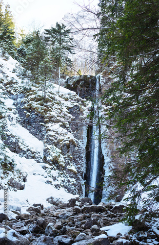 Mountain waterfall with rocks and cliffs covered with snow