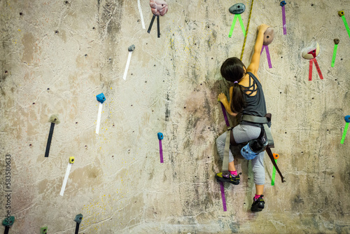 Young asian girl reaching high in indoor rock climbing facility