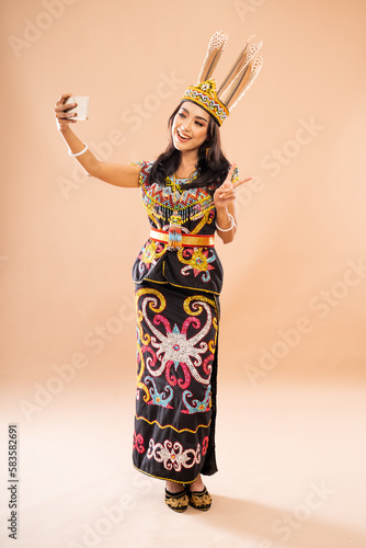 asian woman in king bibinge standing with peace hand gesture while taking selfie photo using the phone on isolated background photo