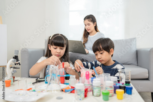 Asian mother looking at her daughter and son doing chemical experiments and tests in living room at home.Home laboratory education science concept for kids.