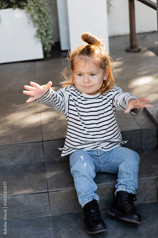 toddler child in casual clothes demanding attention and gesturing while sitting on stairs near house. toddler child in casual clothes demanding attention and gesturing while sitting on stairs near house.