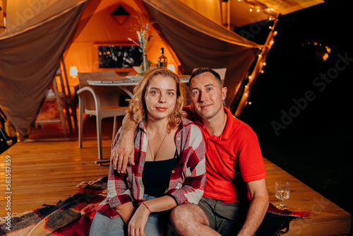 Happy lovely couple relaxing in glamping on evening near cozy bonfire. Luxury camping tent for outdoor recreation and recreation. Lifestyle concept © bondvit