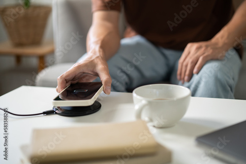 Charging mobile phone battery with wireless charging device in the table. Smartphone charging on a charging pad. Mobile phone near wireless charger Modern lifestyle technology concept.