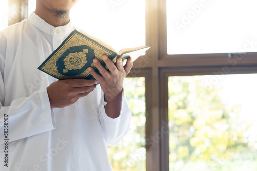 Muslim man reading holy Quran. Holy Quran in Hand with arabic text meaning of Al Quran. Islamic concept background