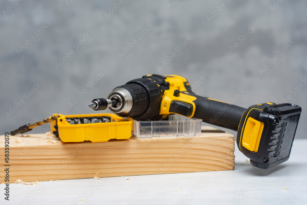 Electric cordless screwdriver on the battery on the table with a self-tapping screw in the board. Electric cordless screwdriver on the battery on the table with a self-tapping screw in the board.
