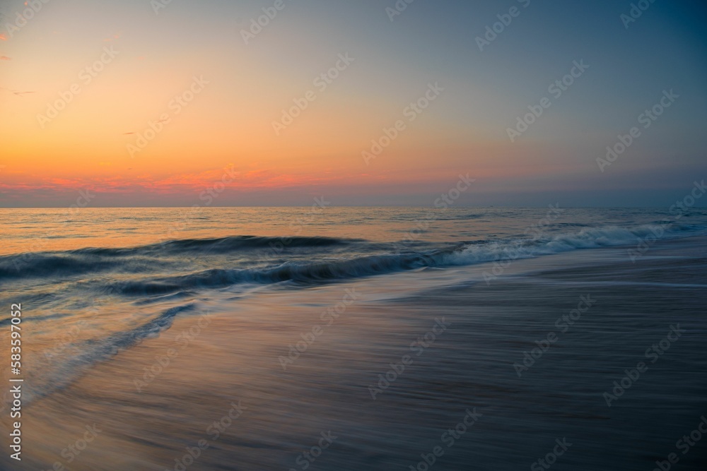 Aerial view of ocean waves breaking beach during sunset